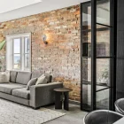 Stylish interior featuring a grey sofa, patterned rug, exposed brick wall, and black steel-framed bifold doors leading to an outdoor view.