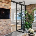 Elegant steel frame bifold doors open to a bright room with lush indoor plants, set against exposed brick walls and a modern decor style.