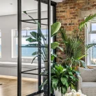 Stylish black steel bifold doors open to a bright space, featuring lush greenery, a textured brick wall, and a sleek sofa.