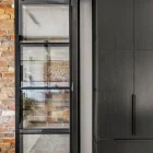A sleek black steel bifold door with glass panels, adjacent to a dark cabinetry section, set against a textured brick wall.