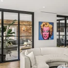Contemporary living room featuring steel-framed glass bifold doors, a vibrant Marilyn Monroe artwork, and lush indoor plants.