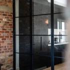 Black steel bifold doors with glass panels, framed in a modern interior with exposed brick walls and a wooden floor.