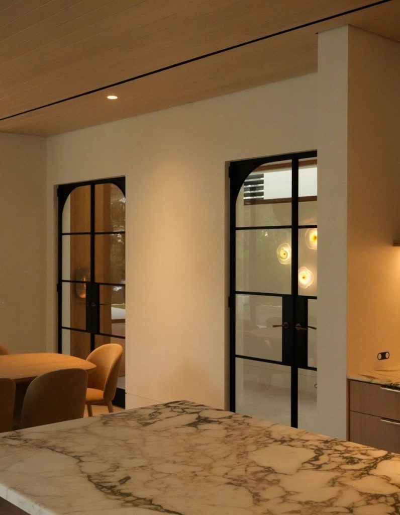 Bespoke architectural steel doors with curved frames, set against warm-toned walls and a marble countertop, creating a modern interior.