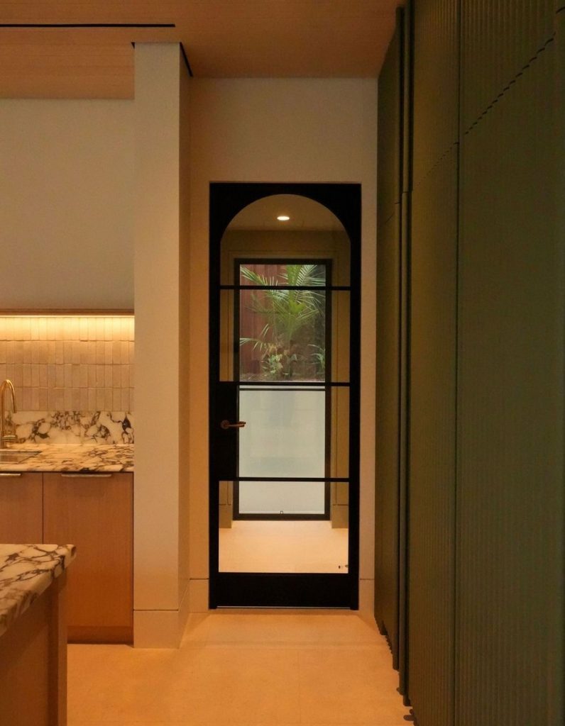 Bespoke black steel door with arched top set against light-coloured walls and green cabinetry, leading to an outdoor space.