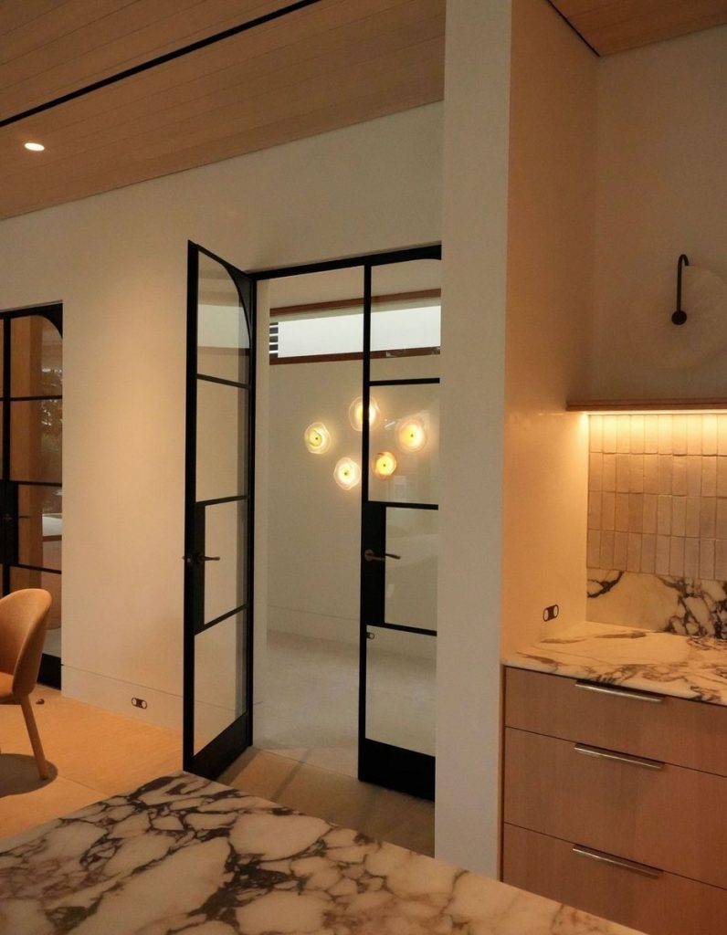 Bespoke architectural steel door in a modern interior with marble countertops, light-coloured cabinetry, and ambient lighting.