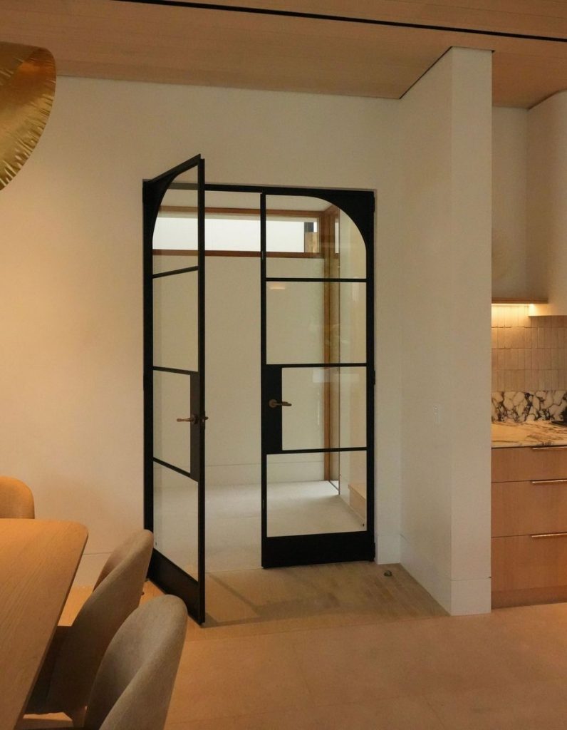 Bespoke black steel-framed door with glass panels, set in a modern interior with light wood accents and minimalistic design elements.
