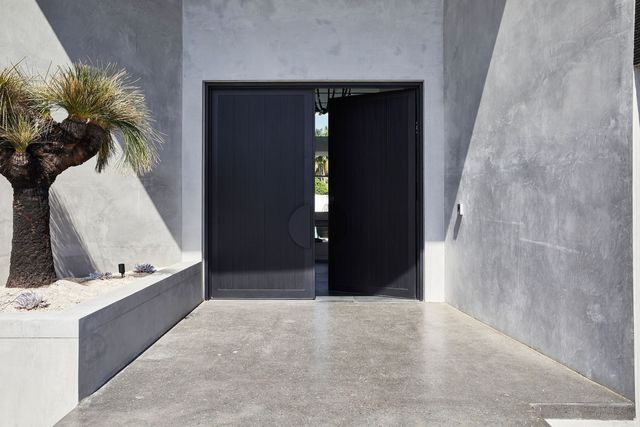 Bespoke Steel Doors at Benfield Concrete House Entrance Bespoke steel double doors open into a modern concrete entryway, featuring a minimalist design and a planted tree accent.