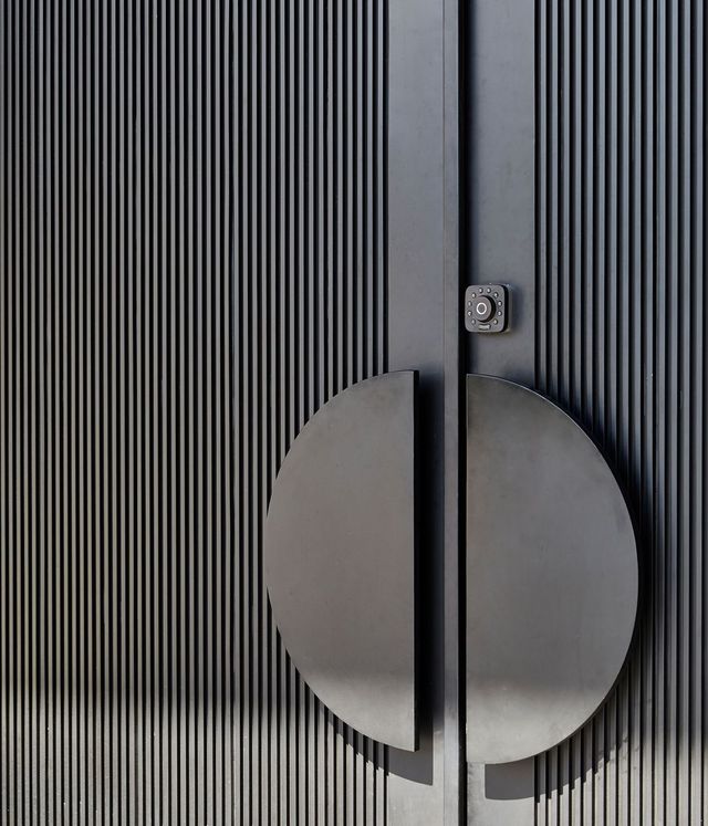Bespoke Steel Doors at Benfield Concrete House Textured black entrance doors featuring a circular handle and smart lock, set against vertical lines for a contemporary architectural look.