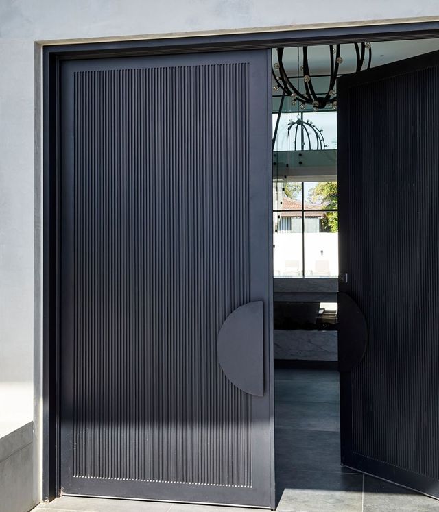 Bespoke Steel Door Design for Contemporary Architecture Sleek black ribbed steel door partially open, revealing an airy interior with minimalistic design and modern lighting.