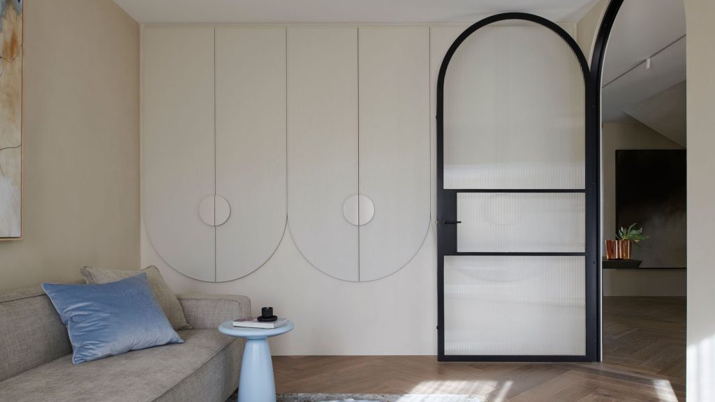 Stylish interior featuring a bespoke black steel-framed door, light-toned walls, curved cabinetry, and a grey sofa with a blue cushion.