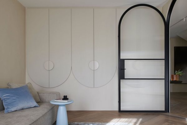 Stylish interior featuring a bespoke black steel-framed door, light-toned walls, curved cabinetry, and a grey sofa with a blue cushion.
