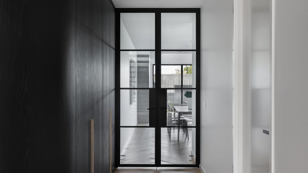 Bespoke black steel-framed doors with large panes, leading to a light-filled space featuring minimalistic design and neutral tones.