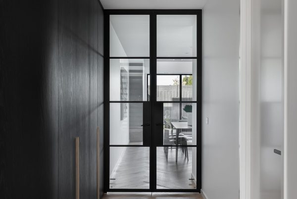 Bespoke black steel-framed doors with large panes, leading to a light-filled space featuring minimalistic design and neutral tones.