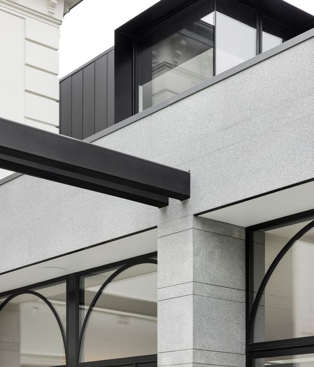 Modern architectural façade featuring sleek steel-framed windows and elegant grey stone detailing, blending contemporary and classic styles.