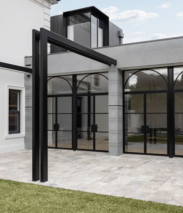 Modern architectural design featuring black steel-framed glass doors with arched tops, set against a light-coloured stone exterior.