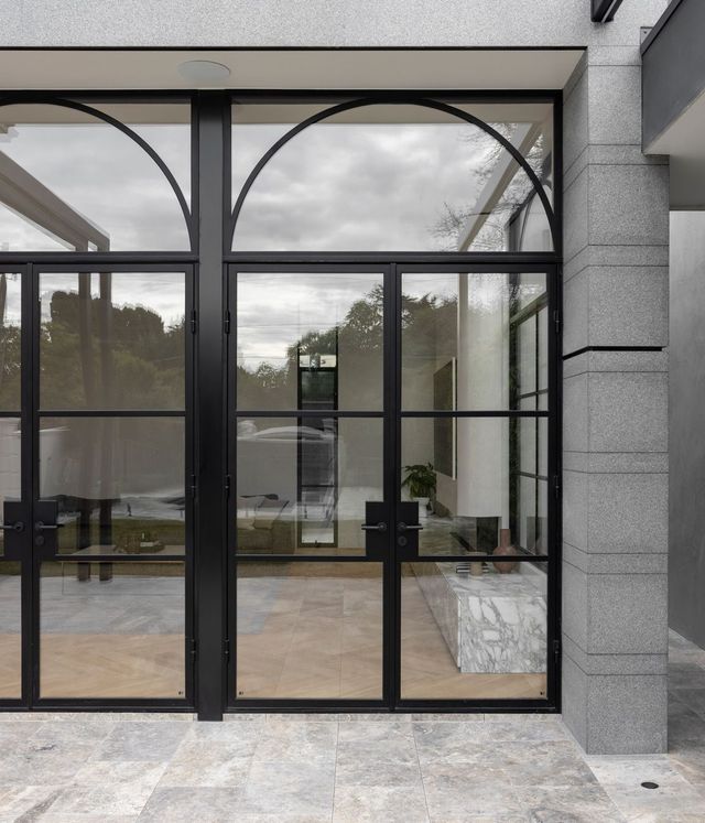 Bespoke steel-framed doors with large arched glass panels, set in a modern grey stone façade, complementing the surrounding landscape.