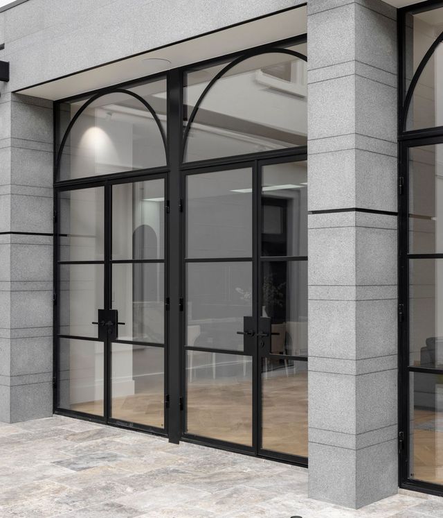 Bespoke black steel doors with arched glass panels, framed by grey stone walls, opening into a contemporary interior space.