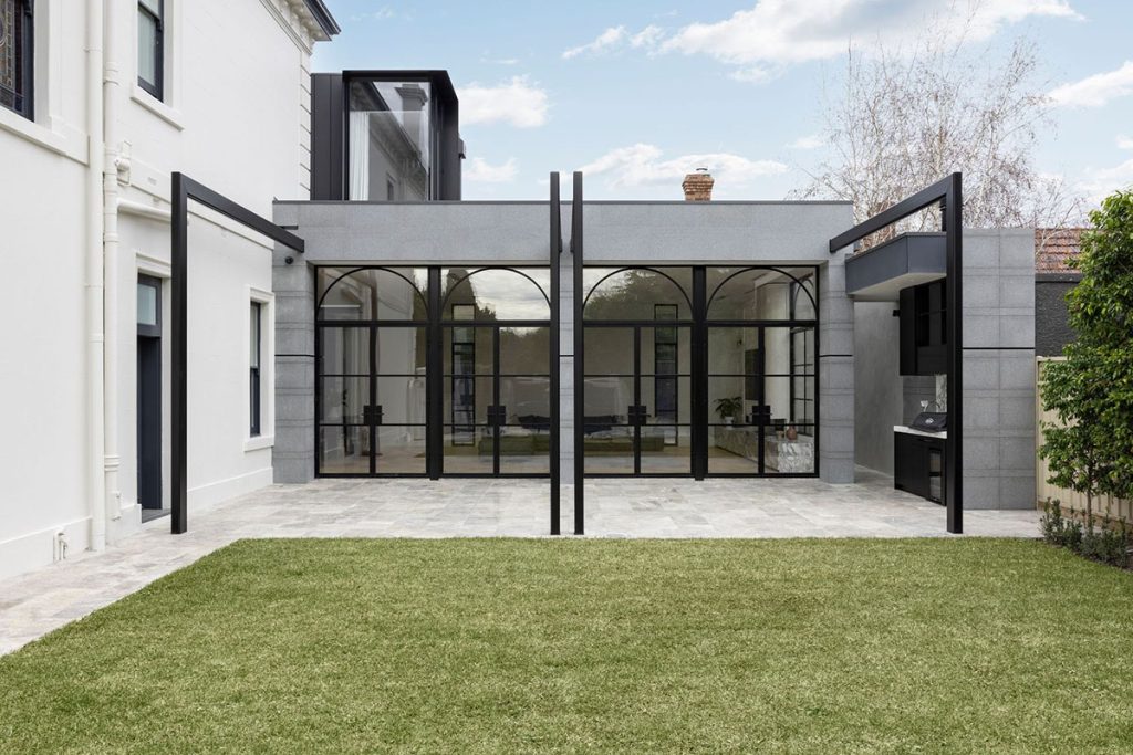 Contemporary grey and black architectural extension with large steel-framed glass doors, overlooking a landscaped garden.