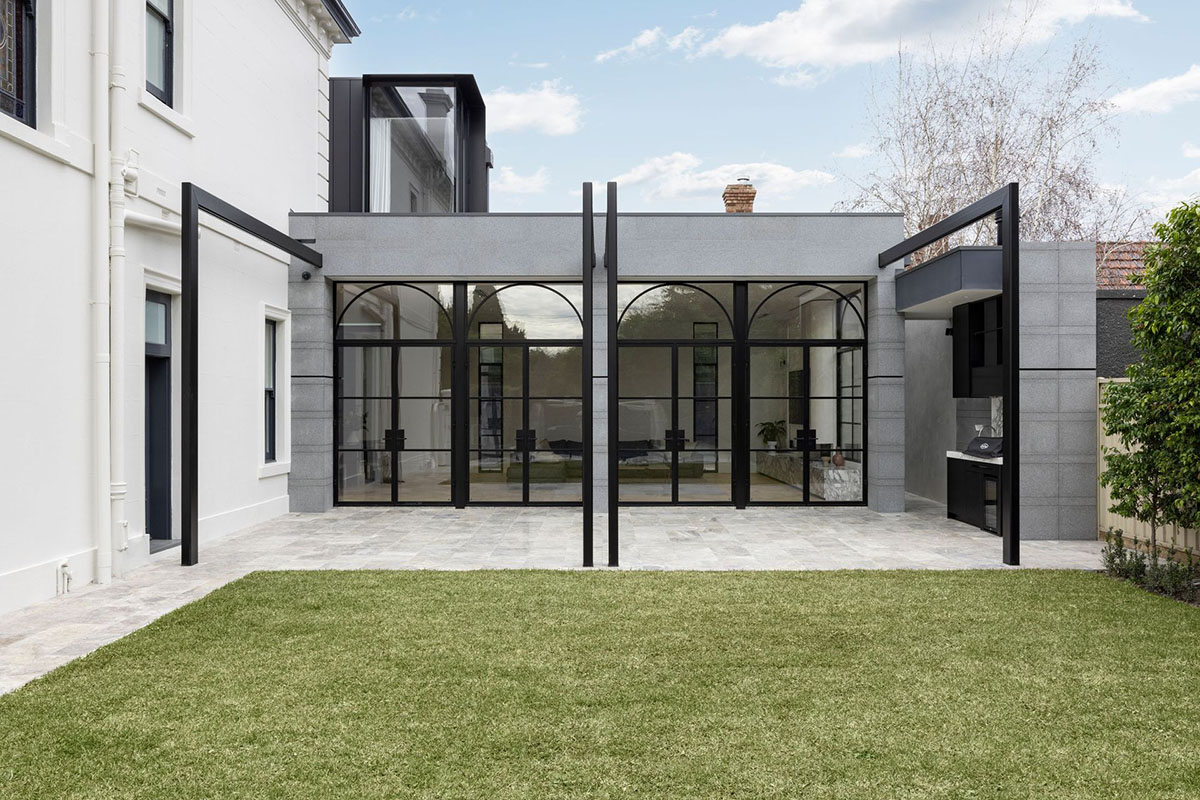 Contemporary grey and black architectural extension with large steel-framed glass doors, overlooking a landscaped garden.