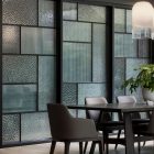 Contemporary dining area featuring black steel-framed bifold doors with textured glass panels, complemented by a wooden table and chairs.