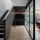 A sleek interior space featuring a glass bifold door with a textured design, leading to a wine storage area beside a modern staircase.