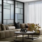 Modern living room featuring a curved olive green couch, a round coffee table with a dark decorative element, and large glazed windows with patterned glass.