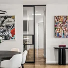 Modern interior featuring a round dining table with flowers, black steel-framed sliding doors, and vibrant art on white walls.