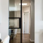 Internal sliding door with a black steel frame, featuring a large glass panel, set in a light, modern hallway with wooden flooring.