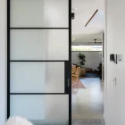 Frosted glass sliding door with a black steel frame, leading into a bright, modern living space with minimalist décor.