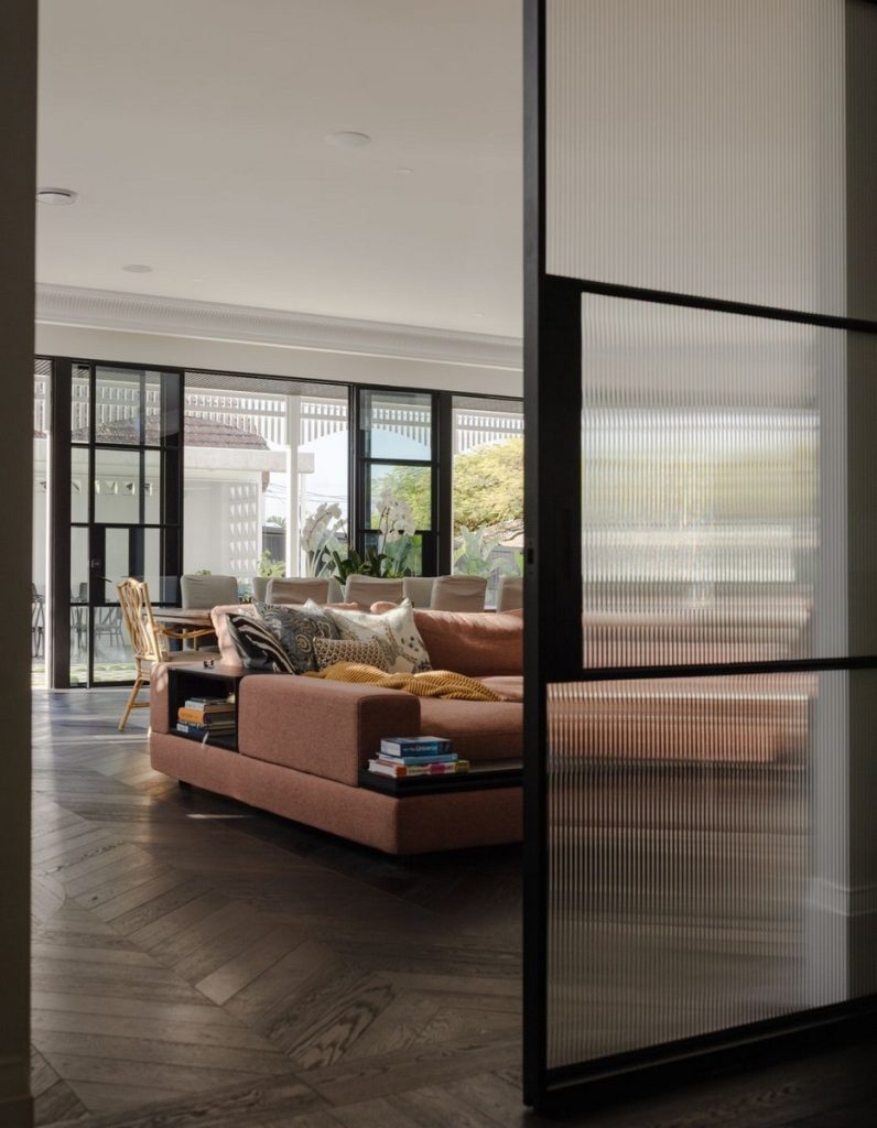 Modern living space featuring a plush brown sofa, large glass windows, and a stylish dining area, with contemporary decor and a warm atmosphere.