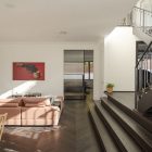 Contemporary living space featuring a pink sofa, wooden dining table, modern artwork, and a staircase leading to an upper level.