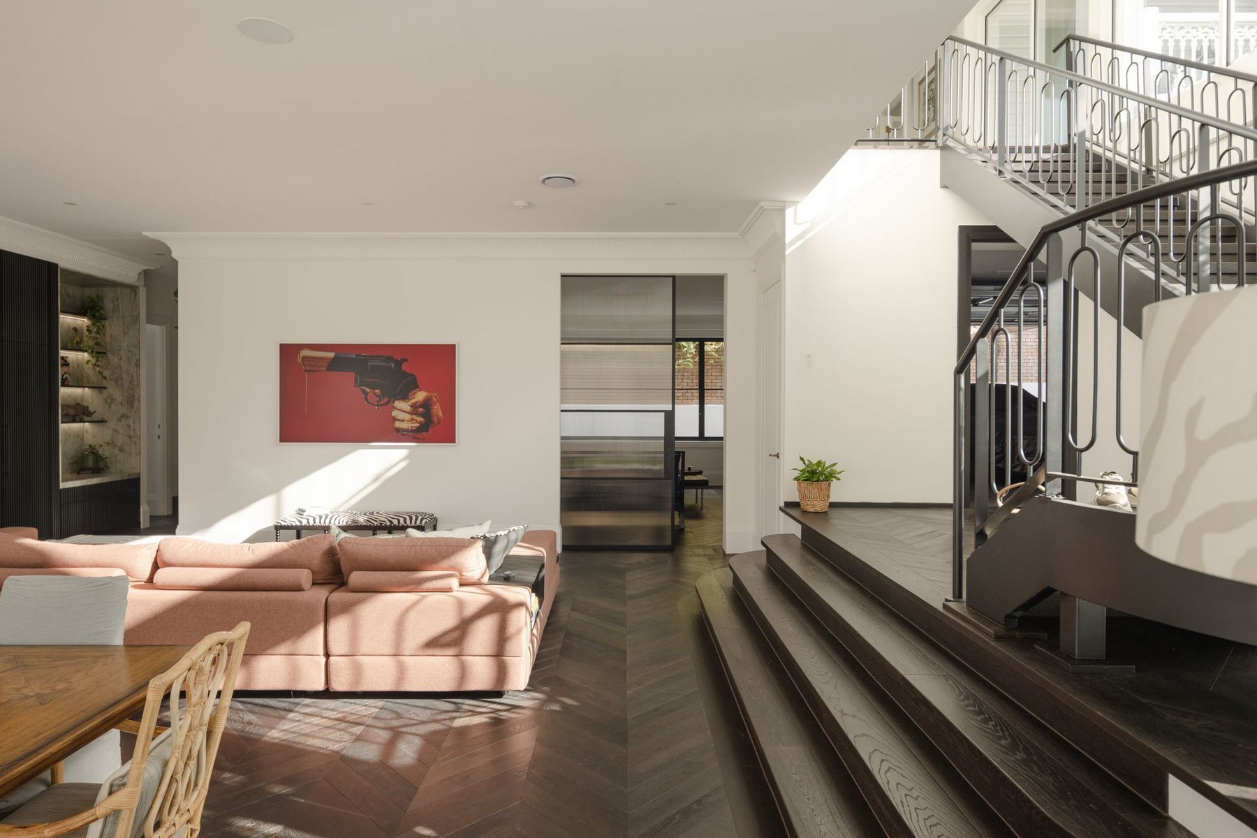 Contemporary living space featuring a pink sofa, wooden dining table, modern artwork, and a staircase leading to an upper level.