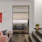 Contemporary interior featuring a steel-framed glass door, a stylish sofa, a bold artwork, and a staircase with dark wood flooring.