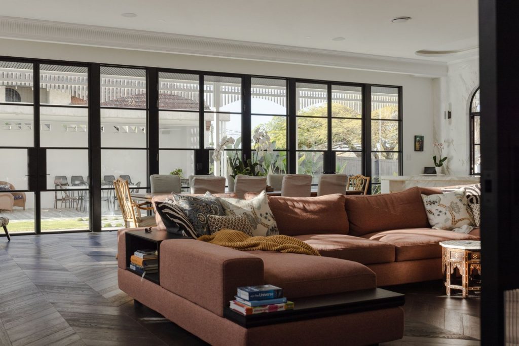 Spacious living room featuring a brown corner sofa, large steel-framed glass doors, and a stylish dining area beyond.
