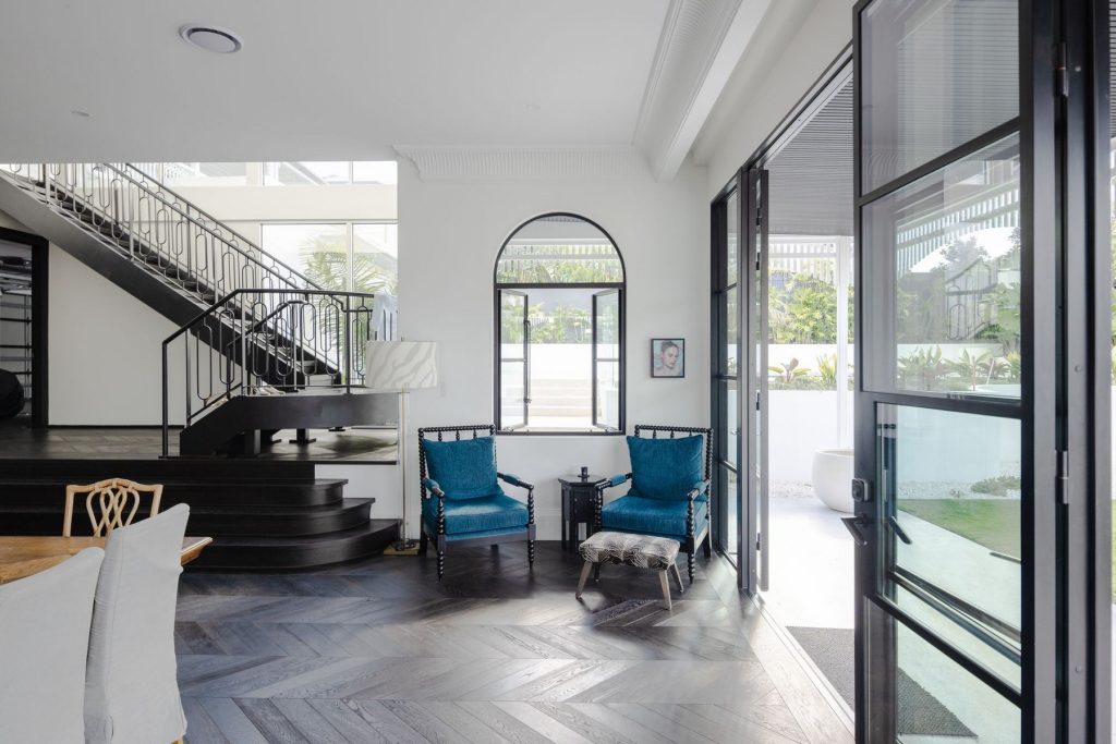 Bright interior featuring black steel-framed doors, elegant staircase, and blue armchairs, creating a modern and inviting atmosphere.
