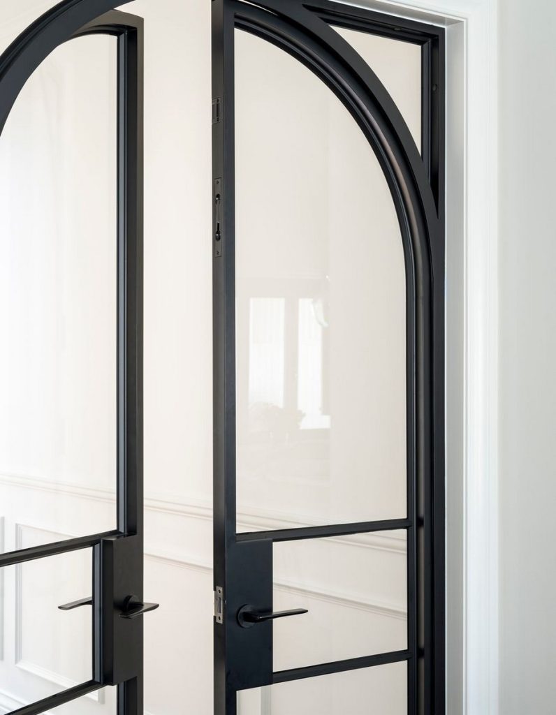 Elegant black steel doors with arched tops and glass panels, set against a light, neutral wall, highlighting seamless design and craftsmanship.