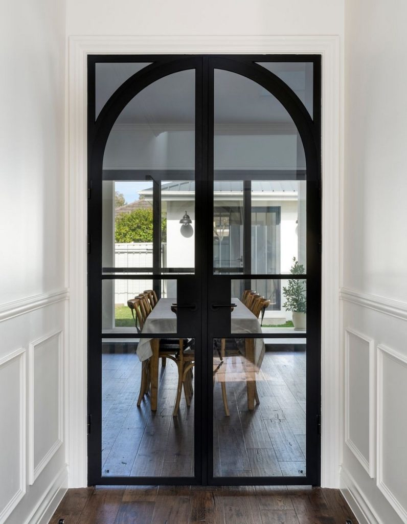 Bespoke black steel arch doors with large glass panels, leading into a bright dining area with a wooden table and chairs.
