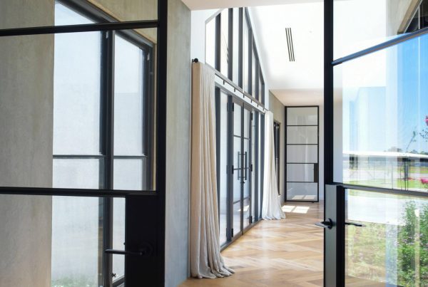 Elegant interior view featuring bespoke steel-framed doors and windows, with light streaming through, complementing the wooden flooring.