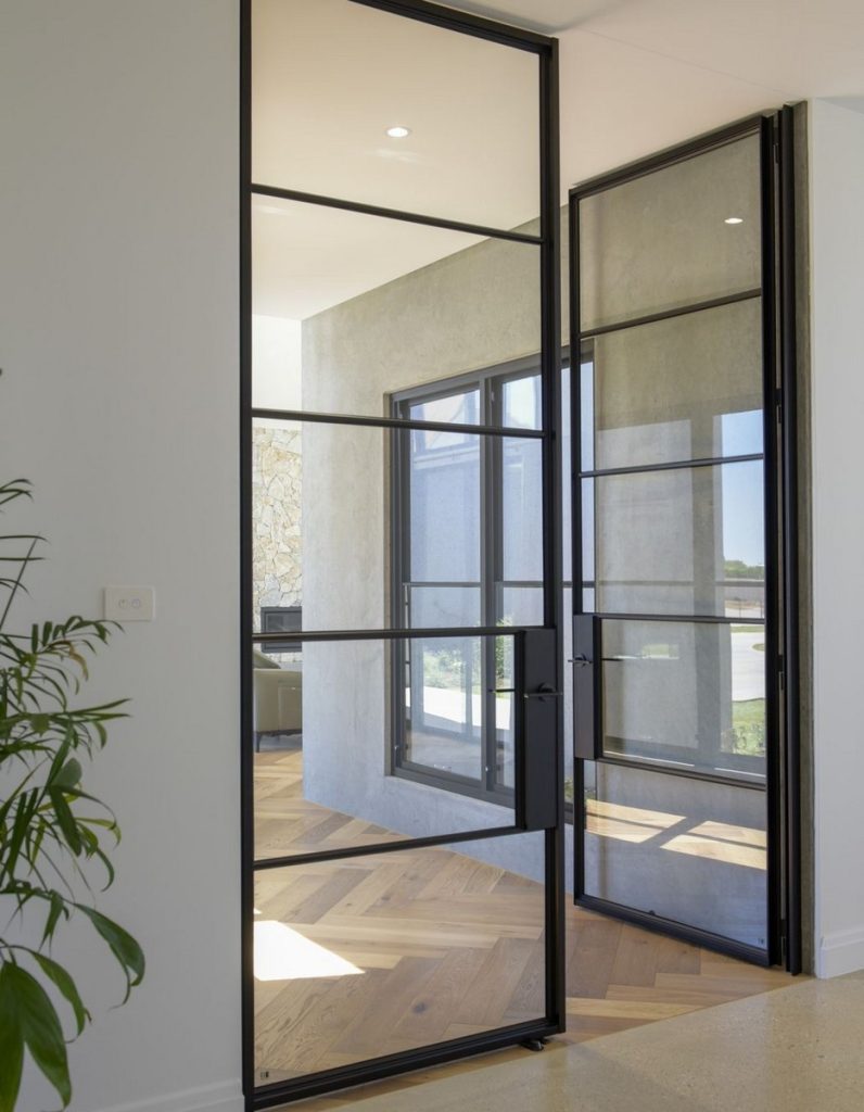 Bespoke black steel-framed double doors, featuring large glass panels, open into a light-filled modern space with wooden flooring.