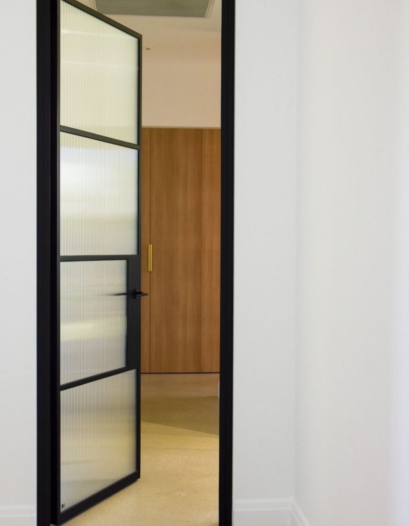 A minimalist interior featuring a steel-framed glass door and a wooden panel door, with neutral tones and clean lines.