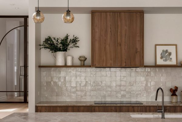 Modern kitchen featuring wooden cabinetry, a textured tile backsplash, and pendant lights, with a glimpse of an arched doorway beyond.