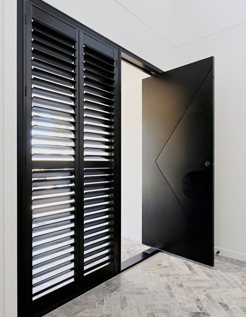 Bespoke architectural steel door with a geometric design, flanked by louvred shutters, set against a light-coloured tiled floor.
