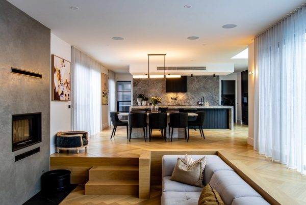 Light-filled interior featuring a modern lounge with a grey sofa, wooden steps, and a sleek kitchen with a marble island and dining area.