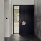 Modern entrance hall featuring a sleek black door with a circular handle, large glass panel, and herringbone wood flooring.