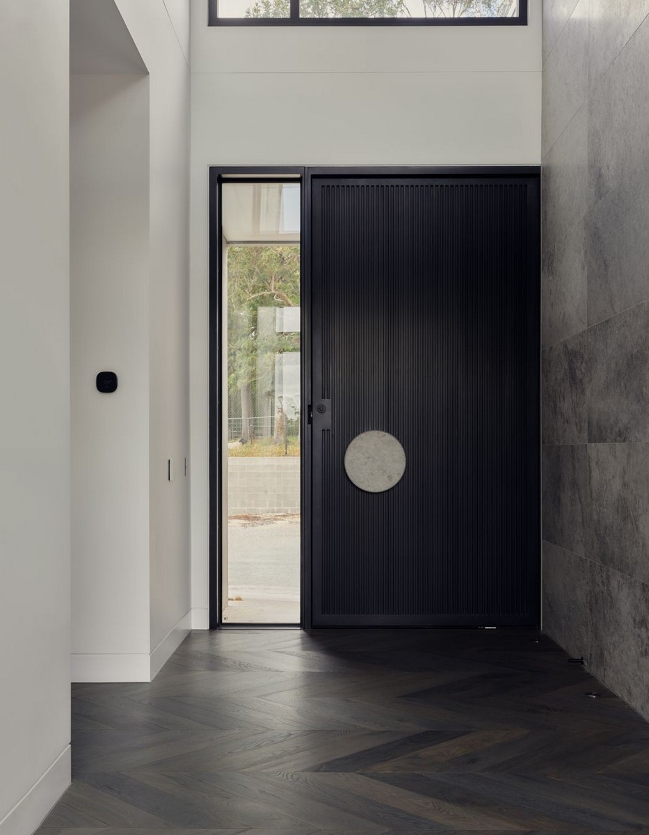 Modern entrance hall featuring a sleek black door with a circular handle, large glass panel, and herringbone wood flooring.