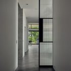 Minimalist corridor featuring vertical steel-framed glass doors with textured panels, grey walls, and herringbone wooden floor.