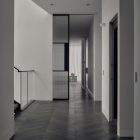 Modern hallway featuring sleek, black-framed glass partitions, light wood flooring, and a minimalist design leading to a softly lit area.