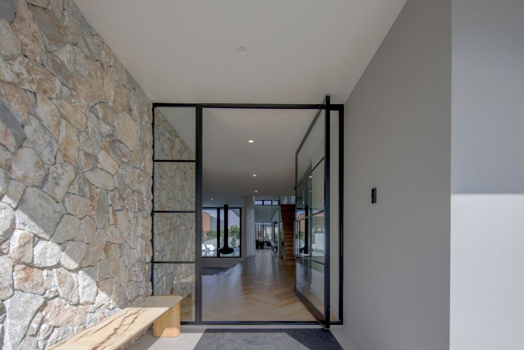Light-filled entrance showcasing a stone feature wall, sleek glass doors, and a wooden bench, leading into an open-plan interior.