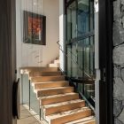 Elegant wooden staircase with steel railings, leading to a glass-fronted upper level, complemented by a vibrant artwork above.