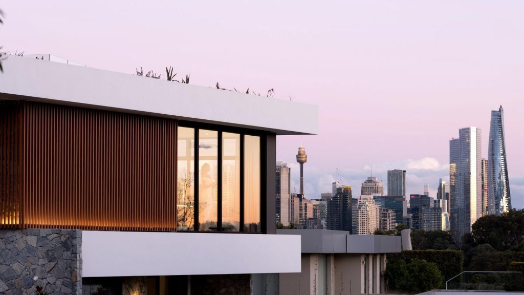 Modern residence featuring sleek architectural lines, large glass windows, and wooden accents, set against a city skyline at dusk.